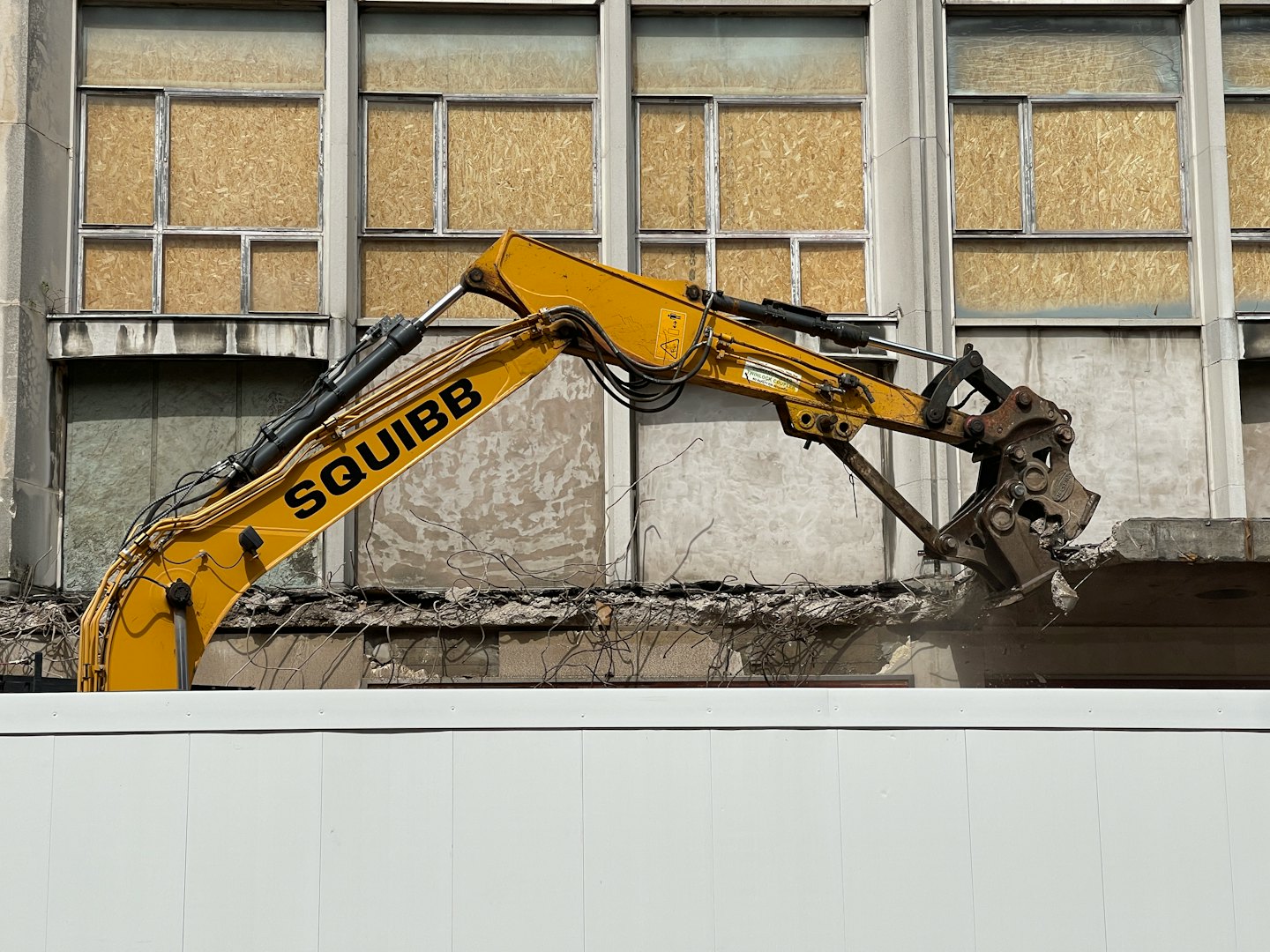 Yellow excavator demolishes concrete building structure.
