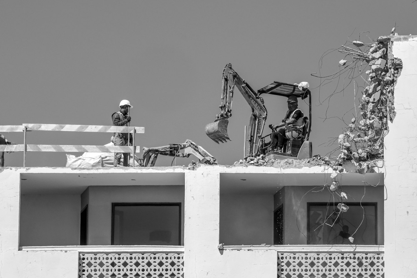 Construction workers demolish a concrete building with a mini-excavator.