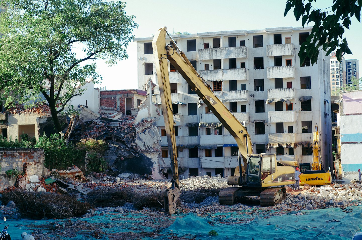 An excavator works on a building demolition site with workers.