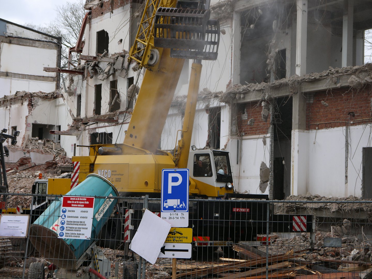 Yellow demolition excavator tearing down a multi-story building.