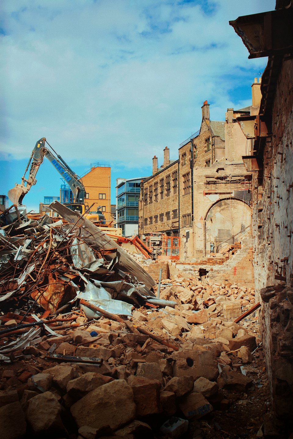 An excavator clears brick and metal rubble at a construction site.