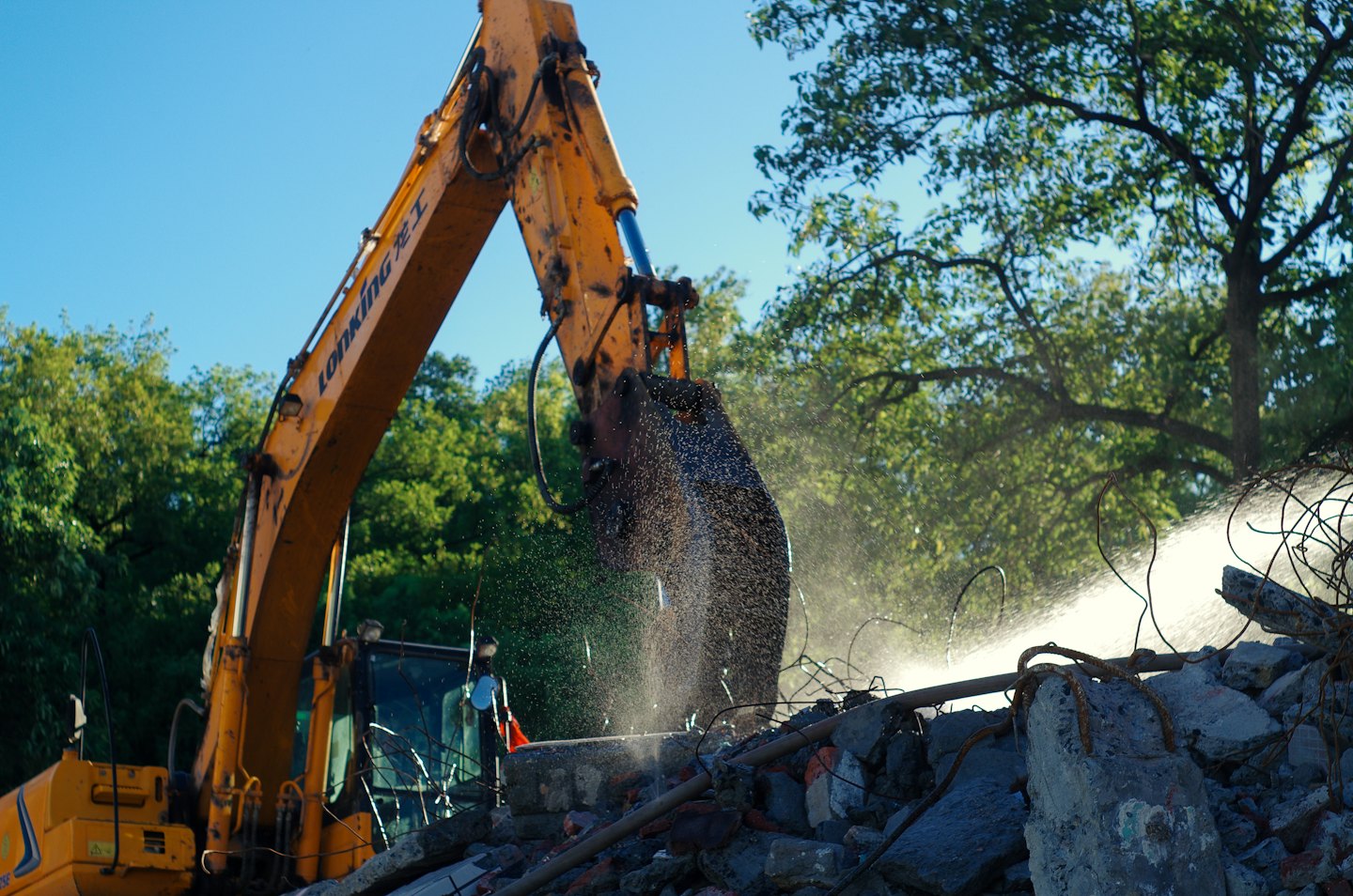 A yellow excavator breaking concrete at a construction site.